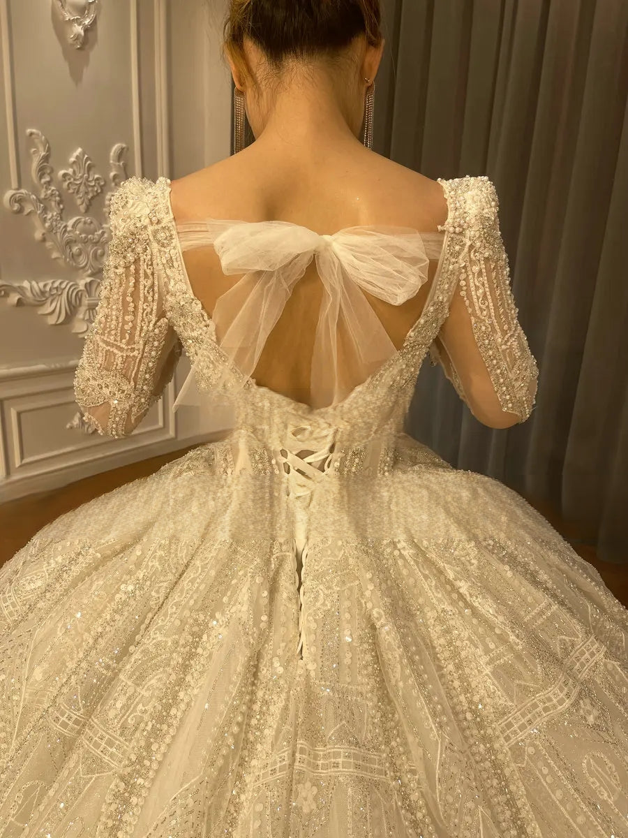 Detailed back view of a beaded wedding gown featuring a deep V-back, a traditional corset lace-up closure, and a large romantic tulle bow at the waist.