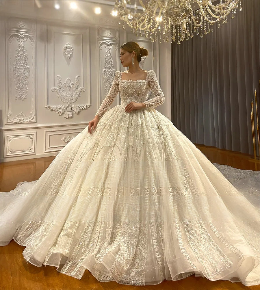 Side profile of a sparkling long train ball gown wedding dress, highlighting the majestic silhouette and grand presence under a crystal chandelier.