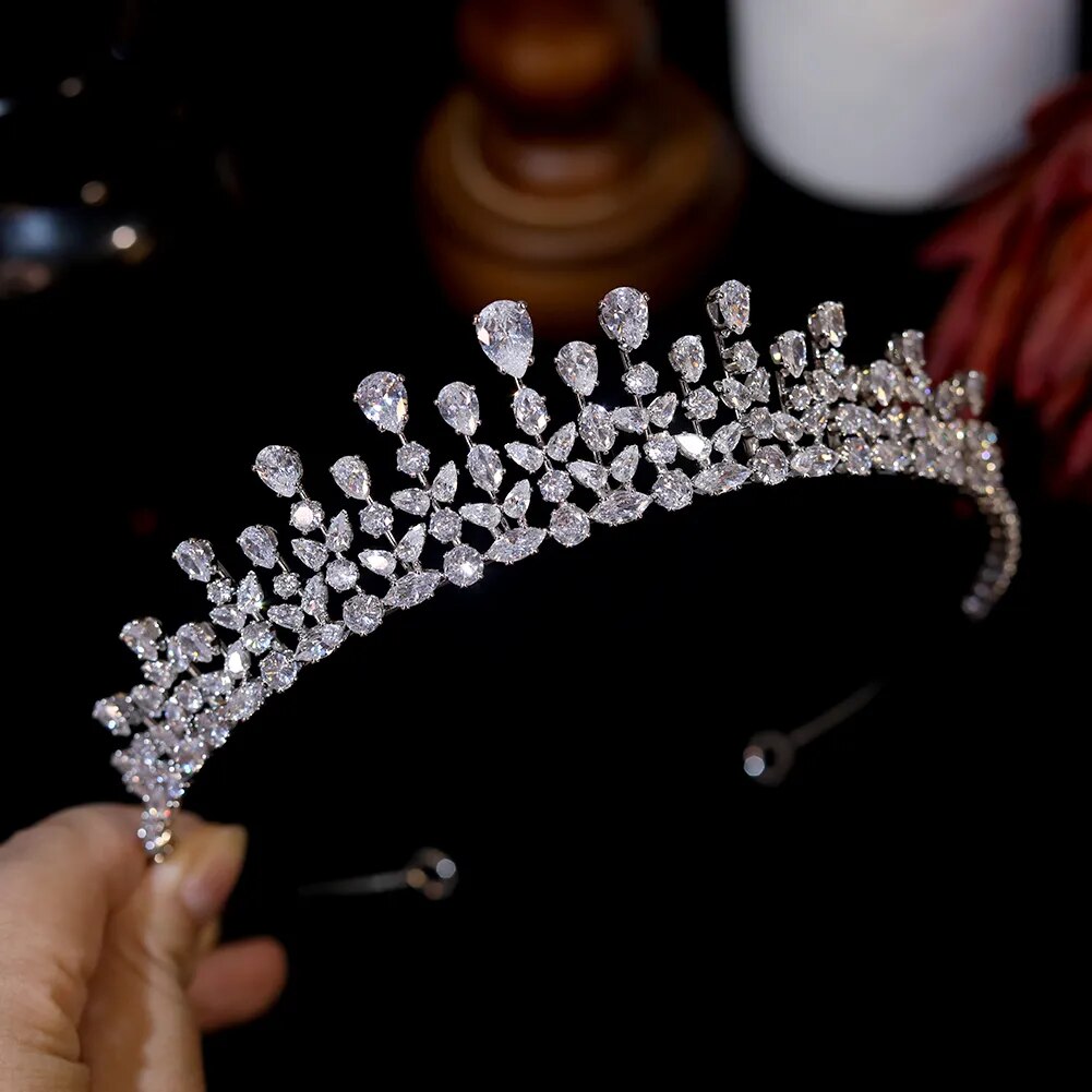 Handheld side profile view of a luxury zircon wedding tiara highlighting tiered rows of micro-pave crystals and teardrop focal points over a black backdrop.
