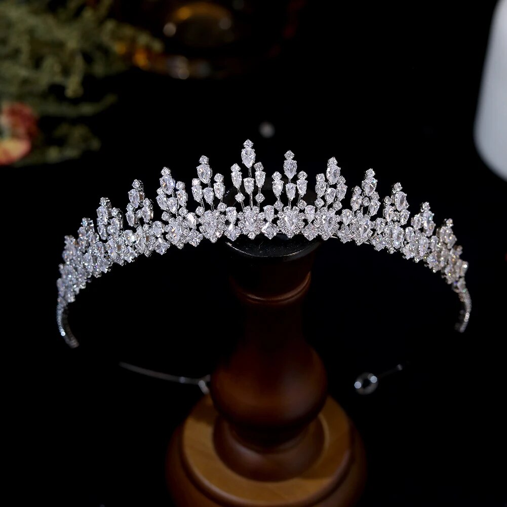 Front perspective of a spike-set princess bridal crown tiara showcased upright on a smooth wooden pedestal jewelry display stand.
