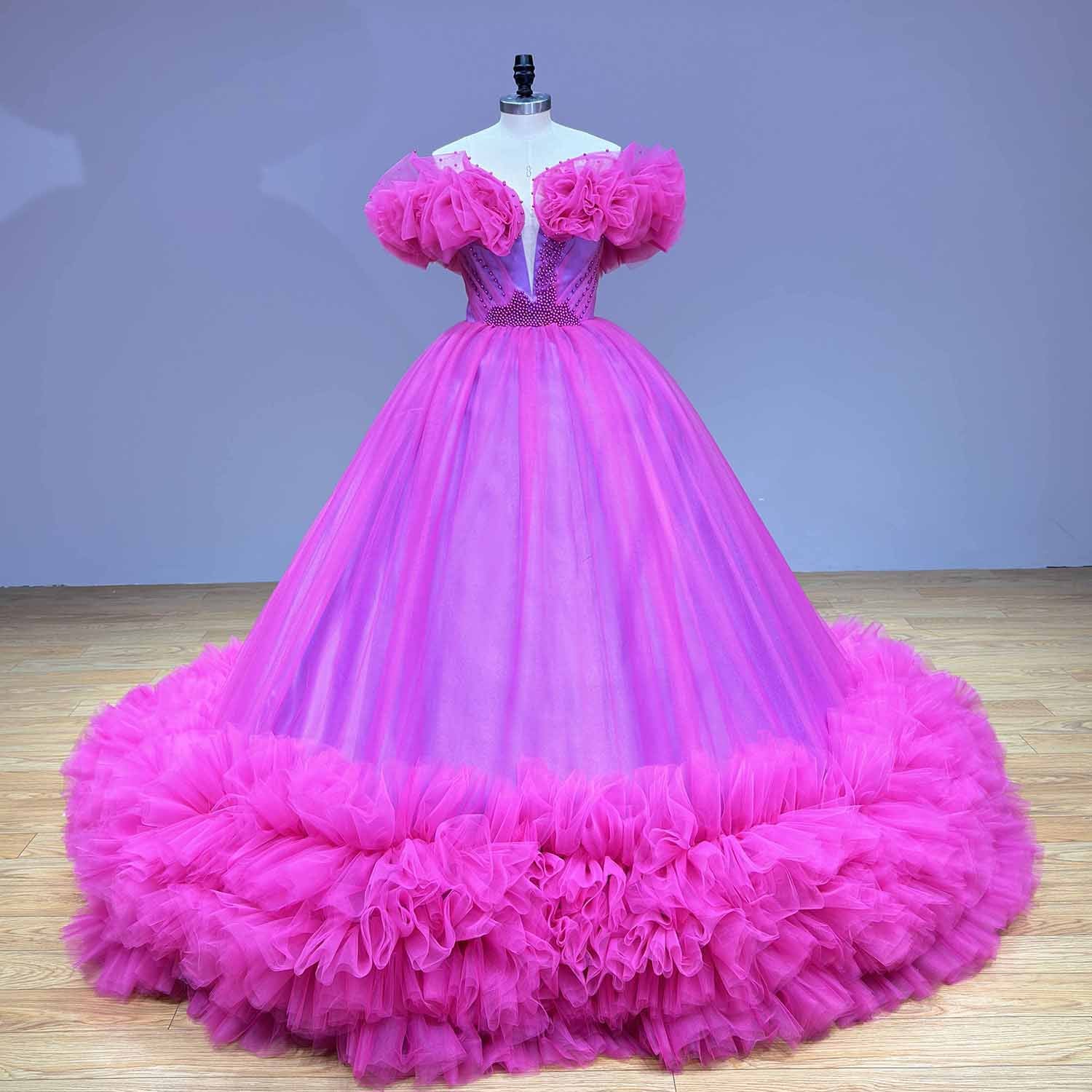 Front view of a couture hot pink tulle ball gown wedding dress featuring a beaded V-neckline and massive ruffled statement sleeves on a studio dress form.