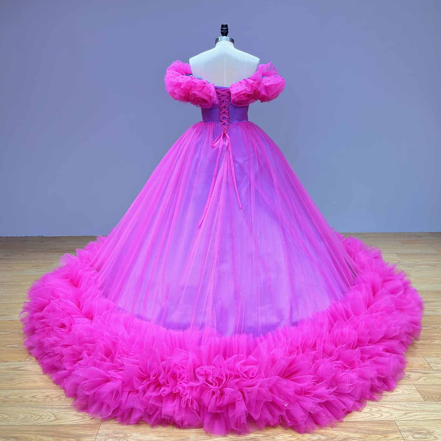 Back view of a magenta pink tulle ball gown showing the adjustable lace-up corset back closure and a wide, voluminous ruffled hemline.