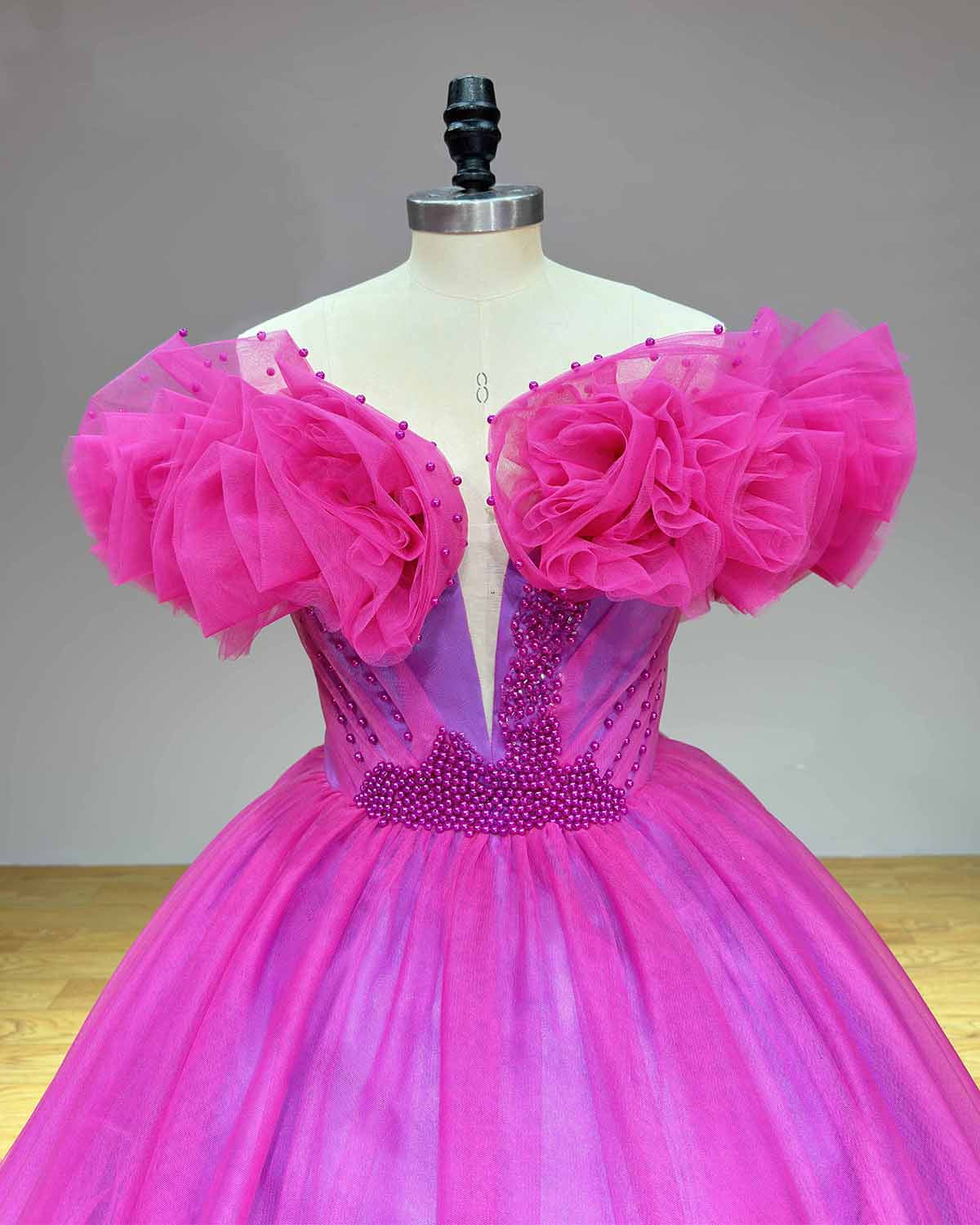 Close-up of the bodice on a fuchsia tulle bridal gown highlighting the intricate purple-pink pearl beadwork along the waistline and a sheer illusion plunge neckline.