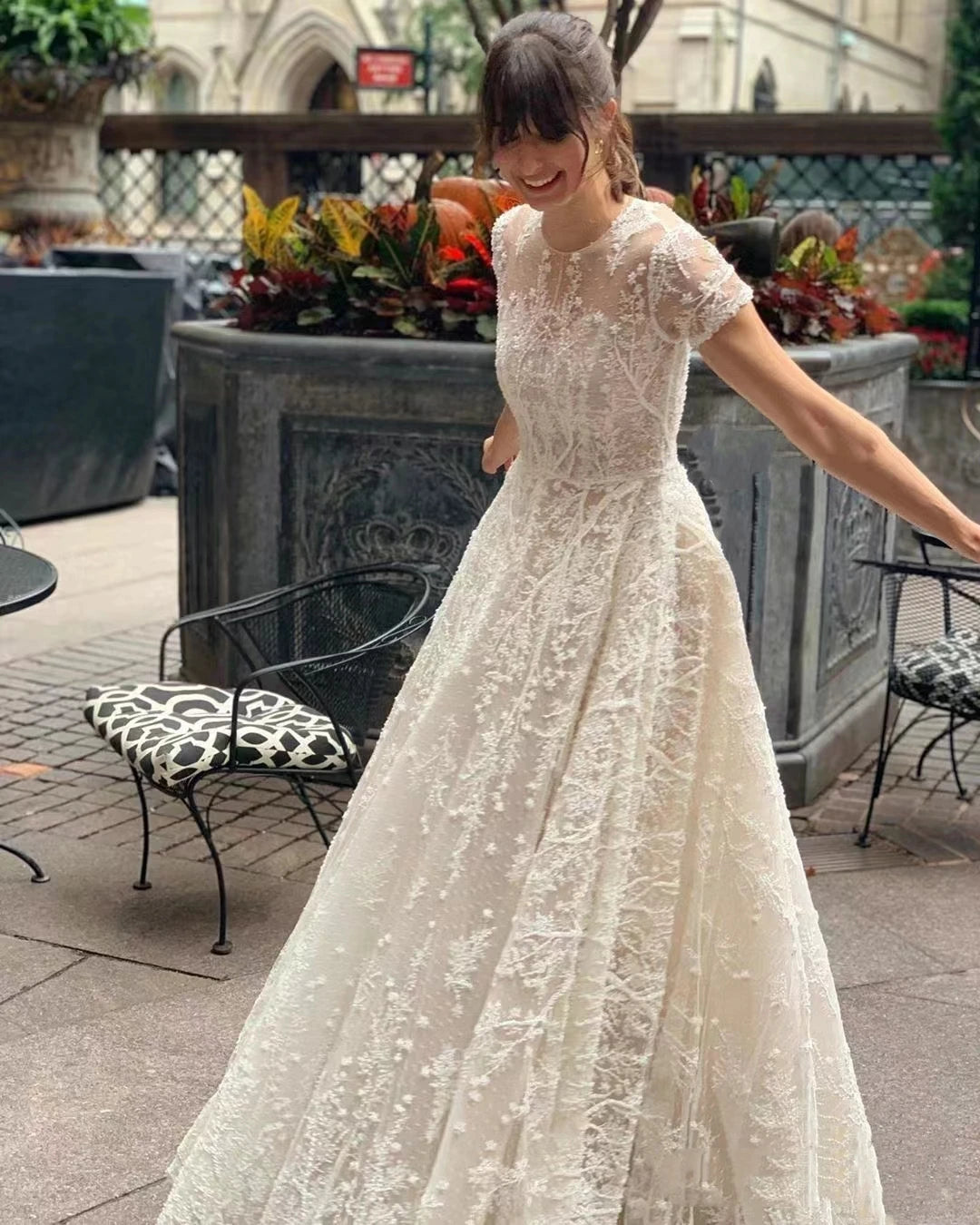 Full-length view of a bride posing in a vintage bohemian wedding dress featuring ornate lace appliqués, short sleeves, and a flowing skirt.