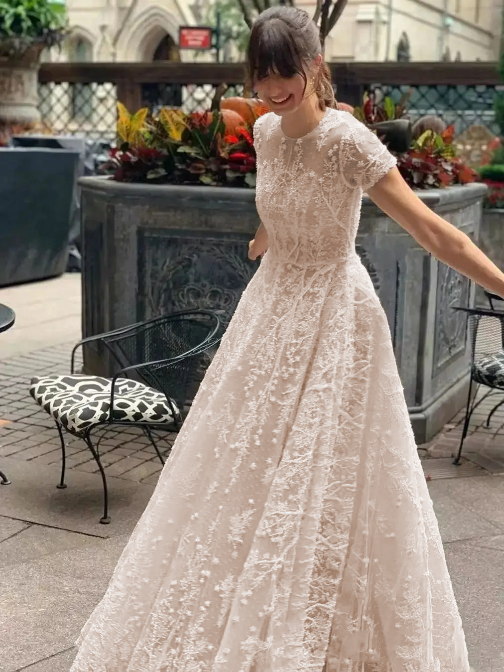 A bride happily twirling in a floor-length lace bohemian wedding dress with short sleeves, captured in a garden setting.