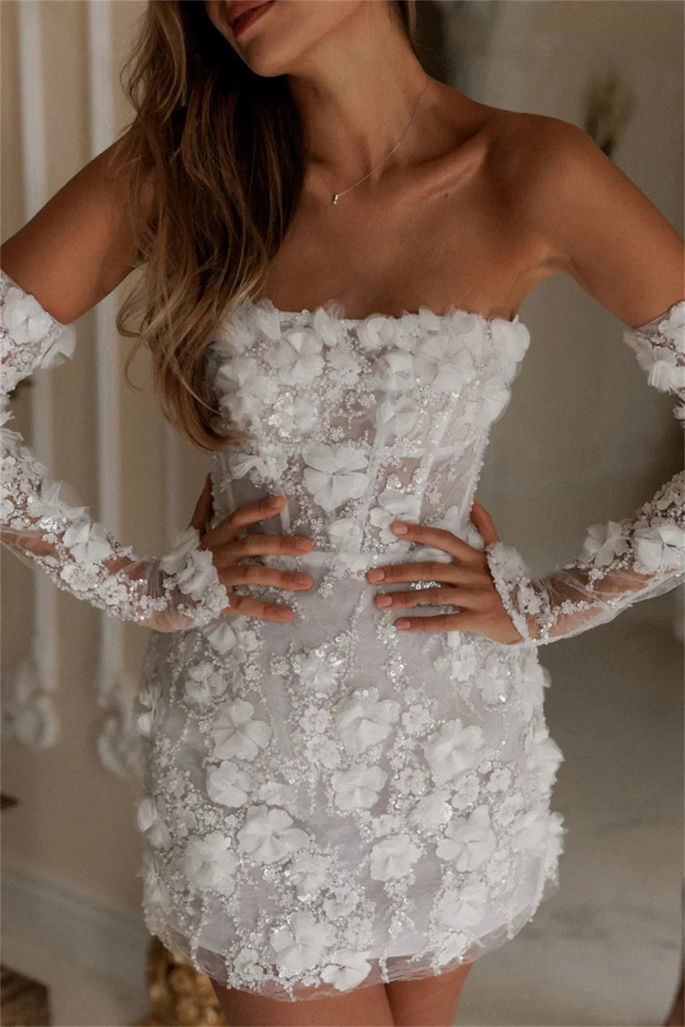 Close-up of a white strapless mini party dress featuring detailed 3D flower embroidery and matching sheer lace long sleeves.