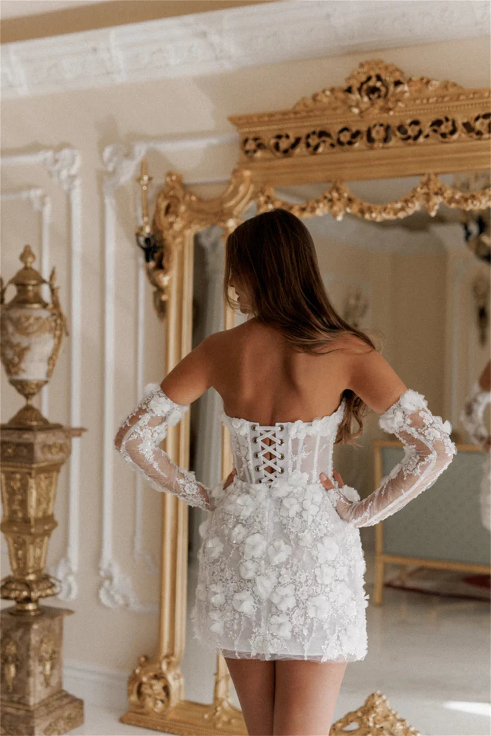 Back view of a white mini dress with 3D floral lace, featuring a corset-style lace-up back and detachable sheer lace sleeves.