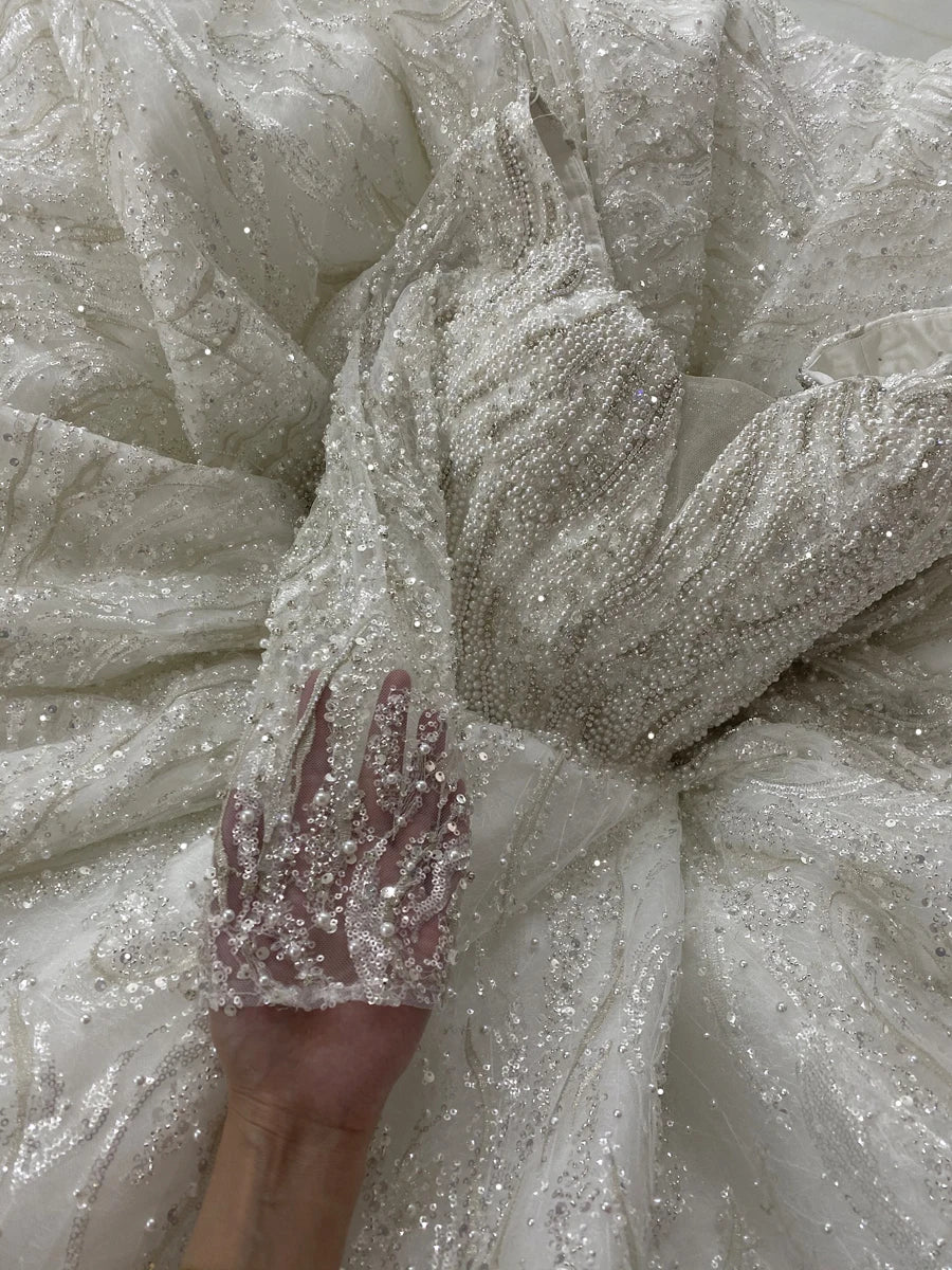 Close-up of a luxury wedding dress bodice highlighting the dense hand-beaded crystal work and shimmering silver sequins on the long sleeves and waist