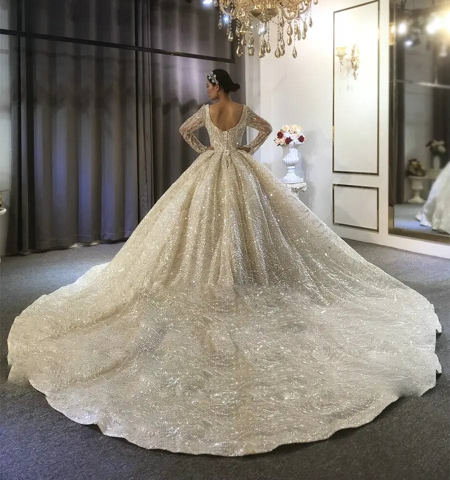 Back view of a full beaded wedding dress on a mannequin, showcasing an elegant lace-up corset back and a massive, shimmering circular cathedral train.