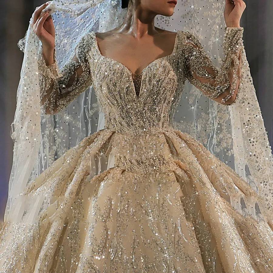 Side profile of a long-sleeve beaded bridal gown, emphasizing the grand volume of the sparkling skirt and the extraordinary length of the royal-style train.