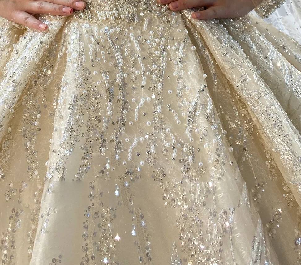 Rear angle of a luxury beaded wedding dress, focusing on the wide-sweep shimmering train and the reflective silver crystal detailing across the cathedral-length fabric.