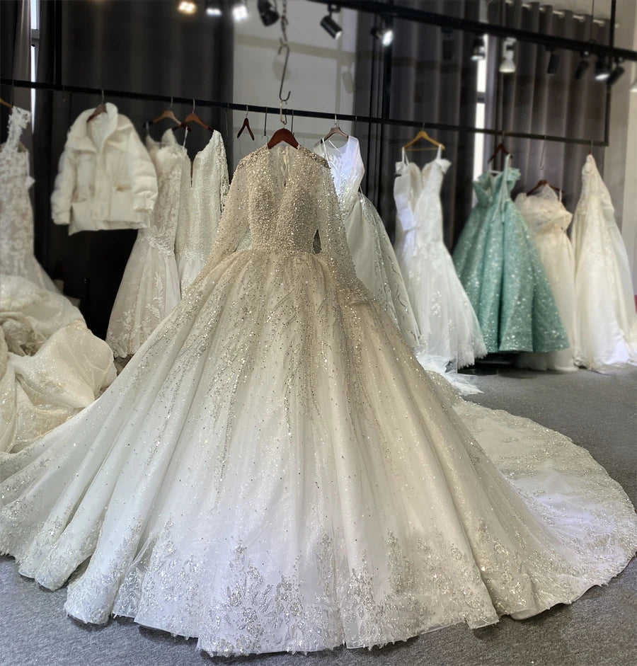 A voluminous luxury bridal ball gown with an elegant long train and intricate pearl beading displayed on a hanger in a professional bridal showroom.