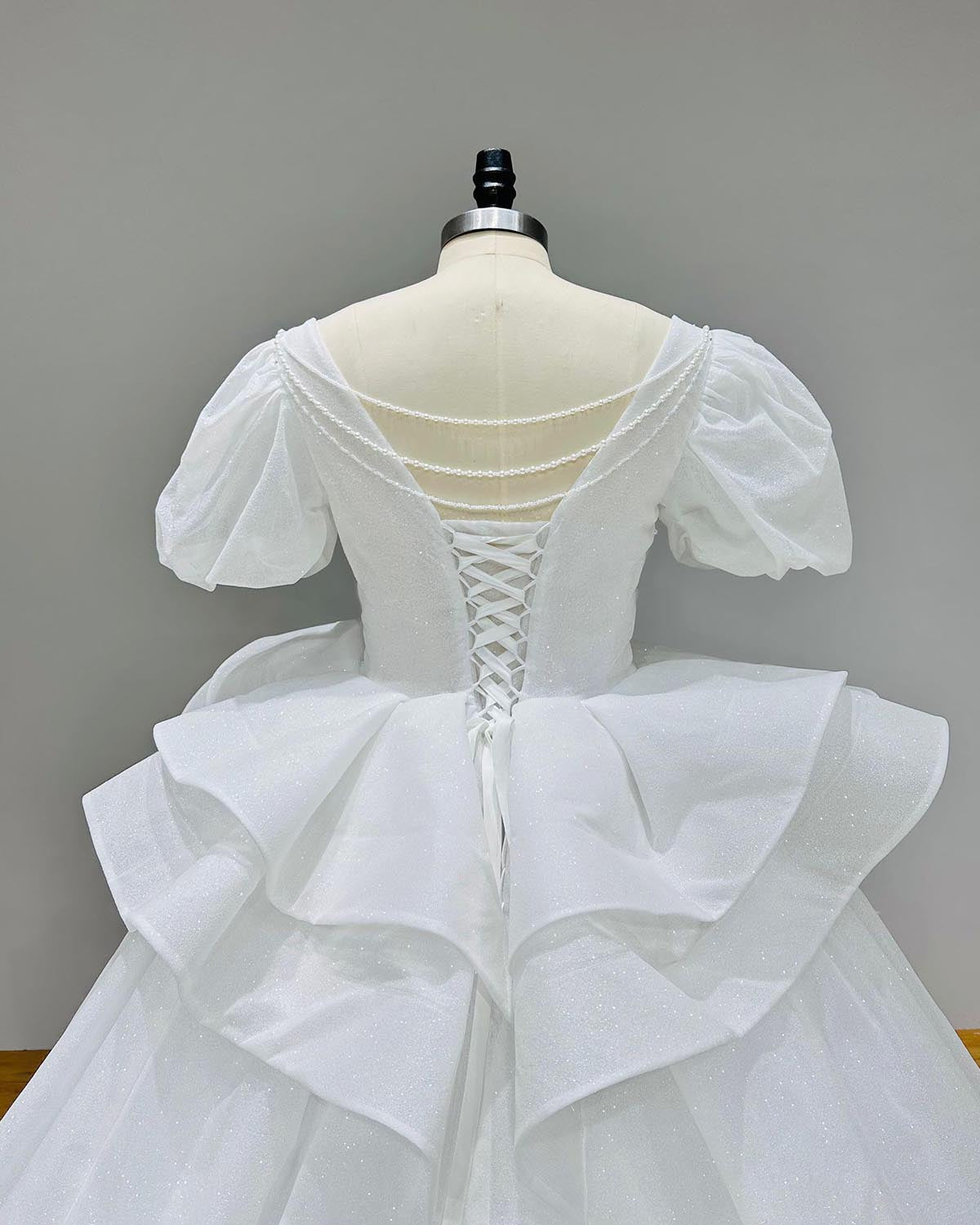 Back view of a luxury glitter wedding ball gown featuring a unique tassel back design and lace-up closure.