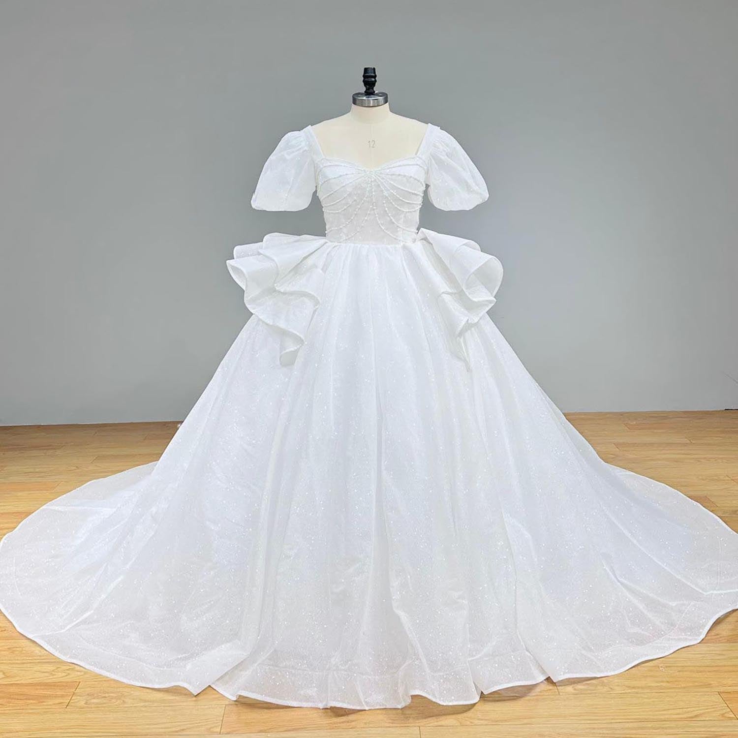 Full-length front view of a luxury glitter short-sleeve bridal ball gown showcasing a dramatic tassel back detail and long train.