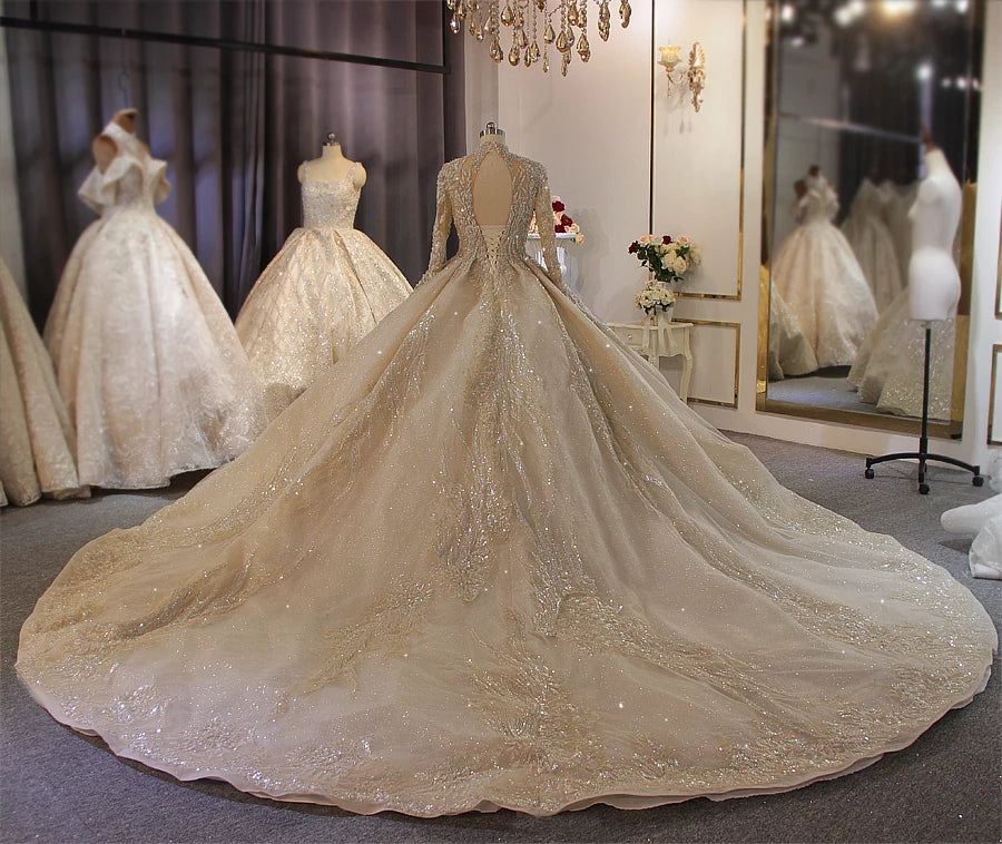 Elegant back profile of a gold long-sleeve bridal gown on a mannequin, showcasing a unique keyhole back design and high-end glitter-patterned lace embroidery.