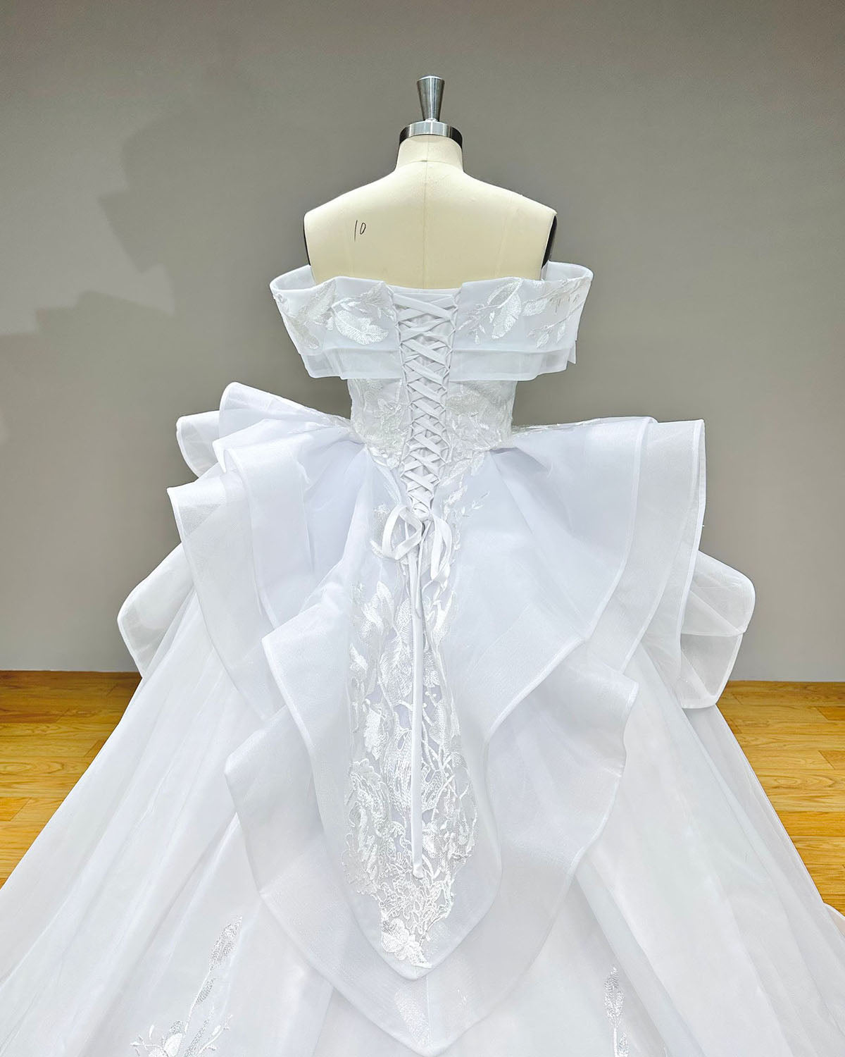 Detailed direct back view of the bridal gown focusing on the satin lace-up corset system, folded off-the-shoulder straps, and tiered cascading organza folds.