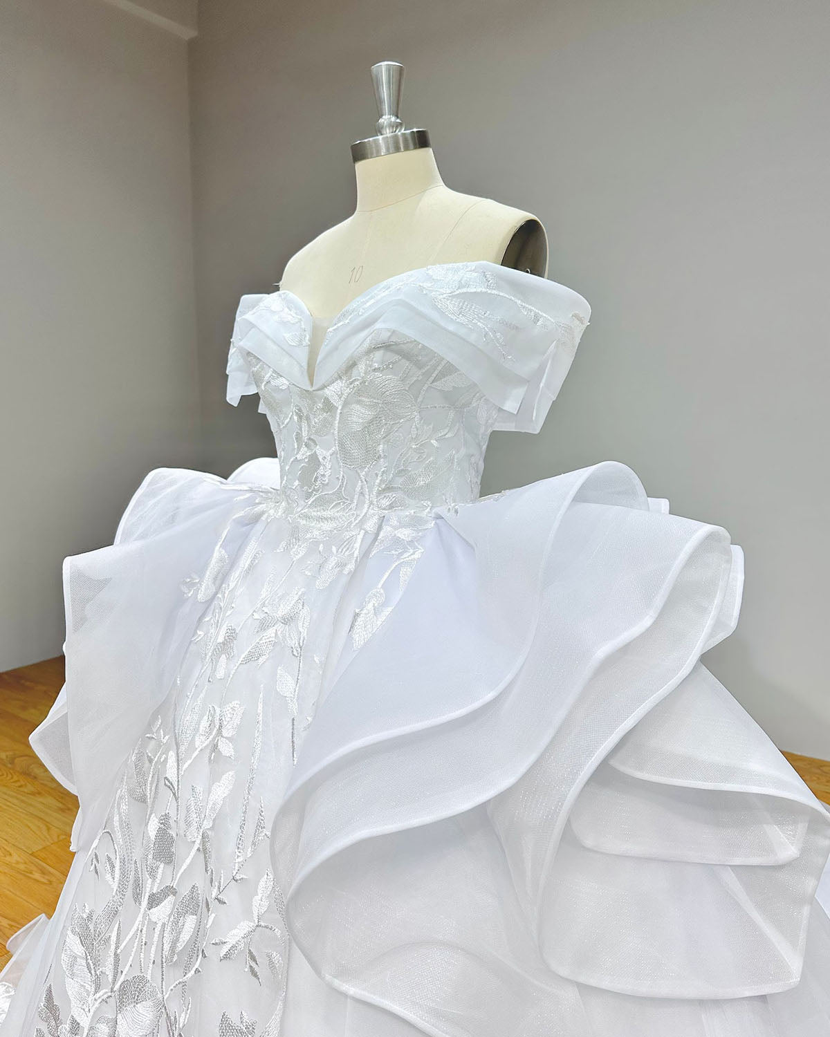 Close-up side front profile of the wedding gown bodice on a mannequin, highlighting the plunged sweetheart neck, floral lace appliques, and statement hip drapes.