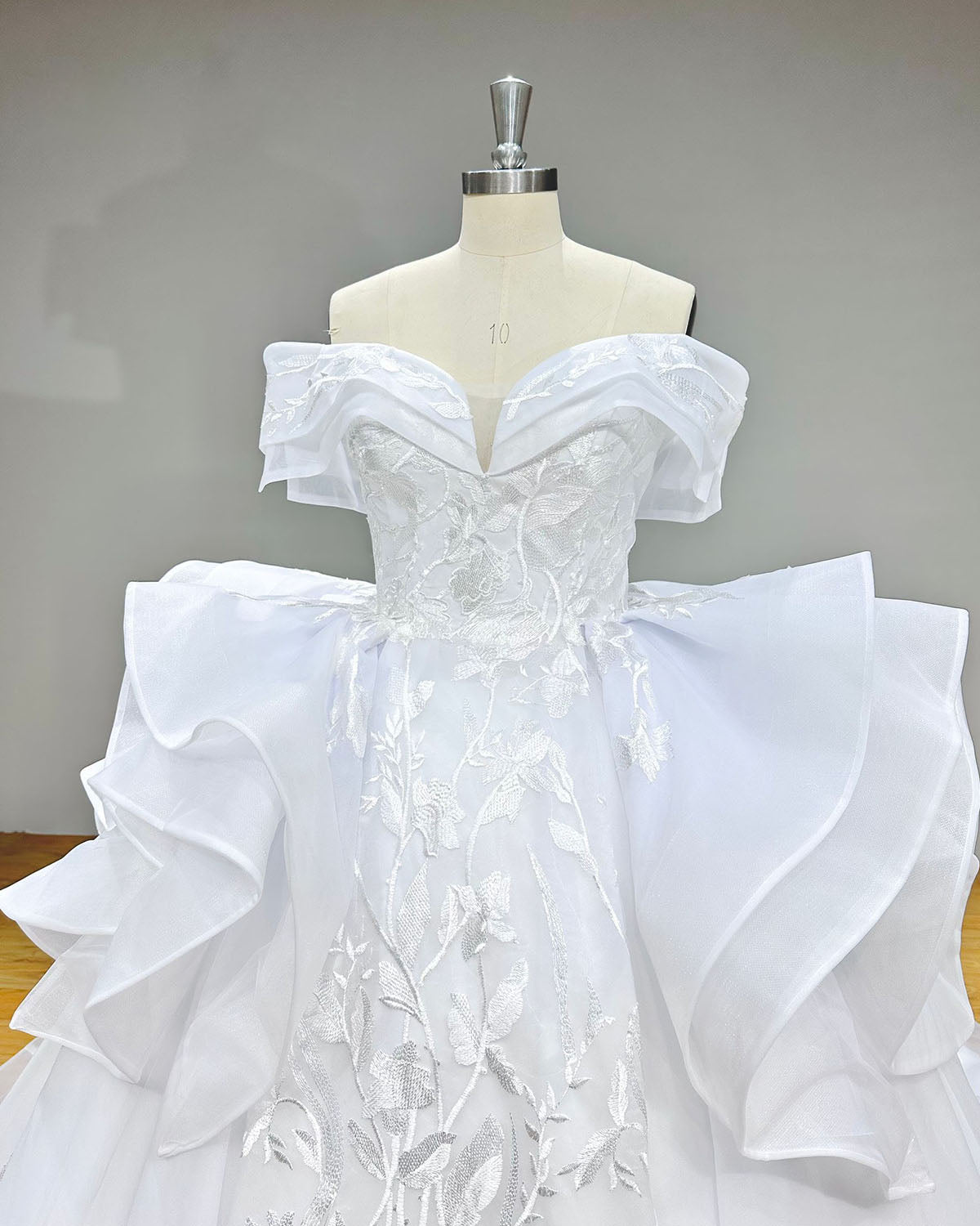 Detailed close-up front shot of the bridal bodice showcasing the folded off-the-shoulder portrait neckline, illusion mesh plunging neckline, and textured white embroidery.