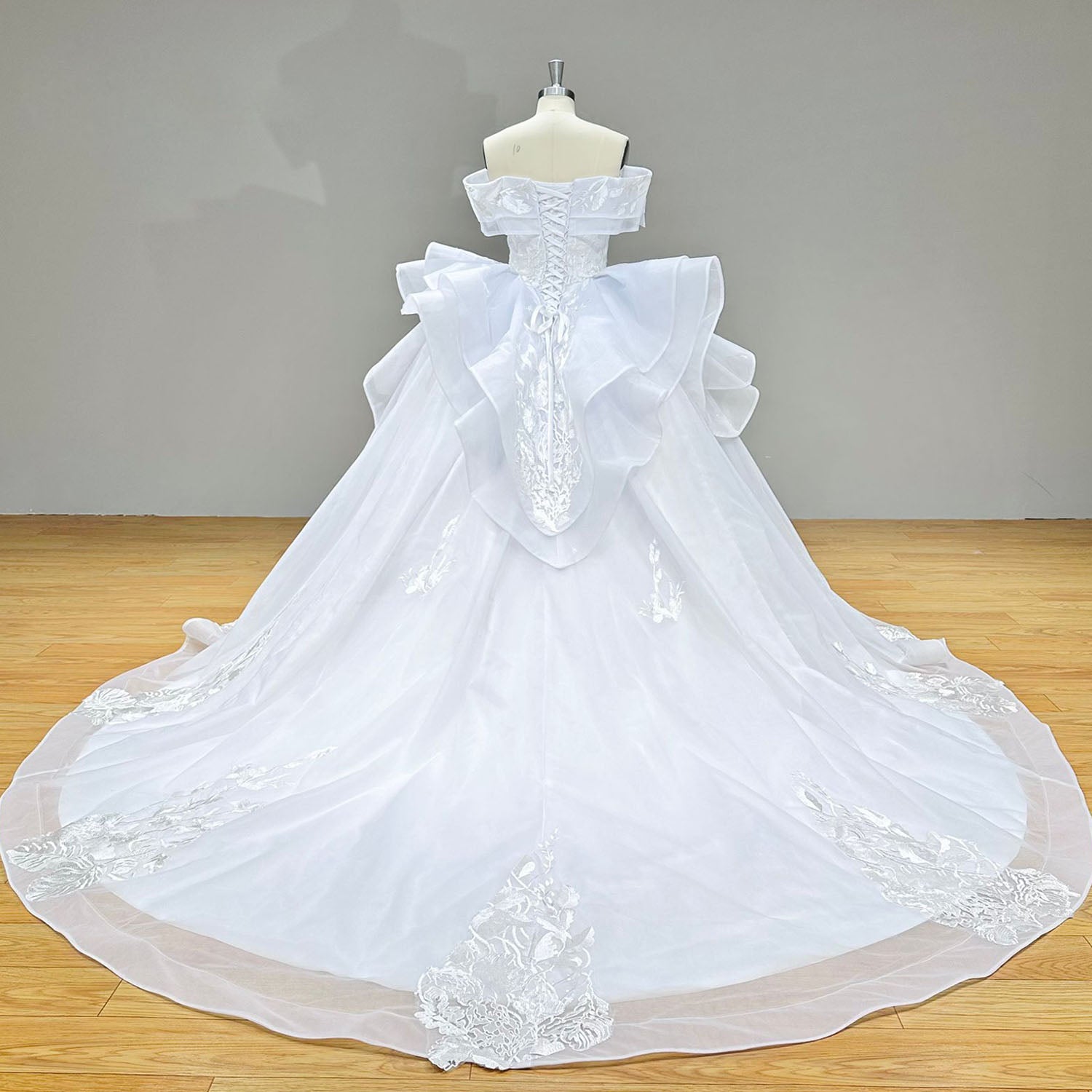 Full-length back view of the luxury wedding gown on a mannequin, highlighting the intricate corset lacing and a massive cathedral-length train with floral lace borders.