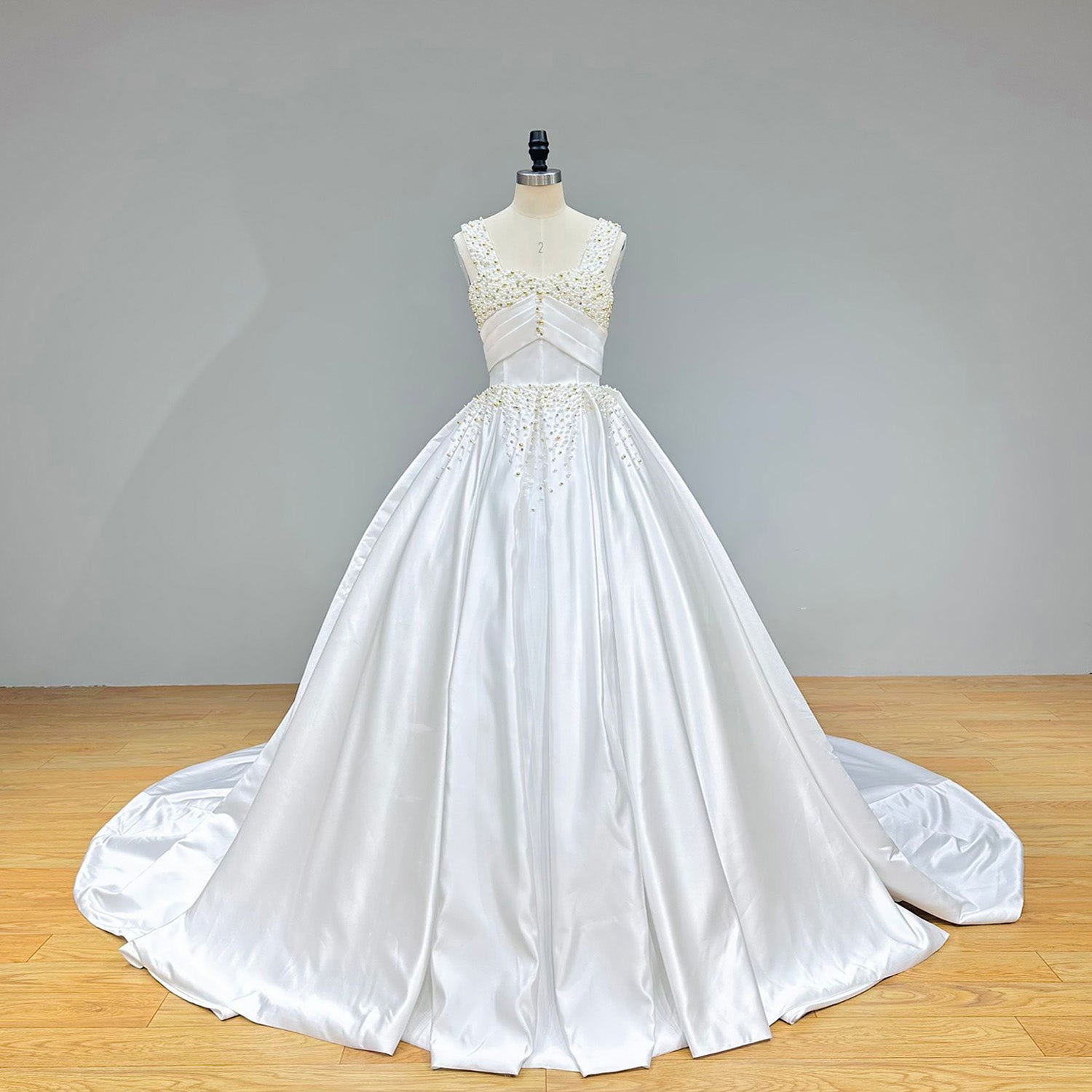 Full-length front view of a structured satin ball gown bridal dress on a dress form, showcasing a sweetheart neckline beneath wide beaded shoulder straps.
