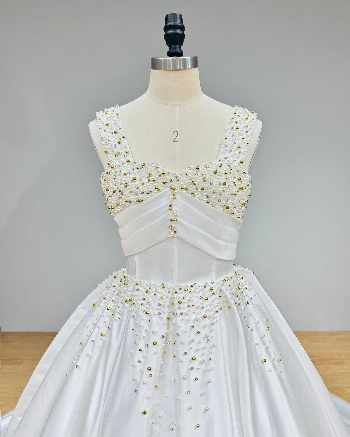 Studio back view of a white satin wedding gown on a dress form, showcasing a majestic sweeping circular train with button details cascading down the center seam.