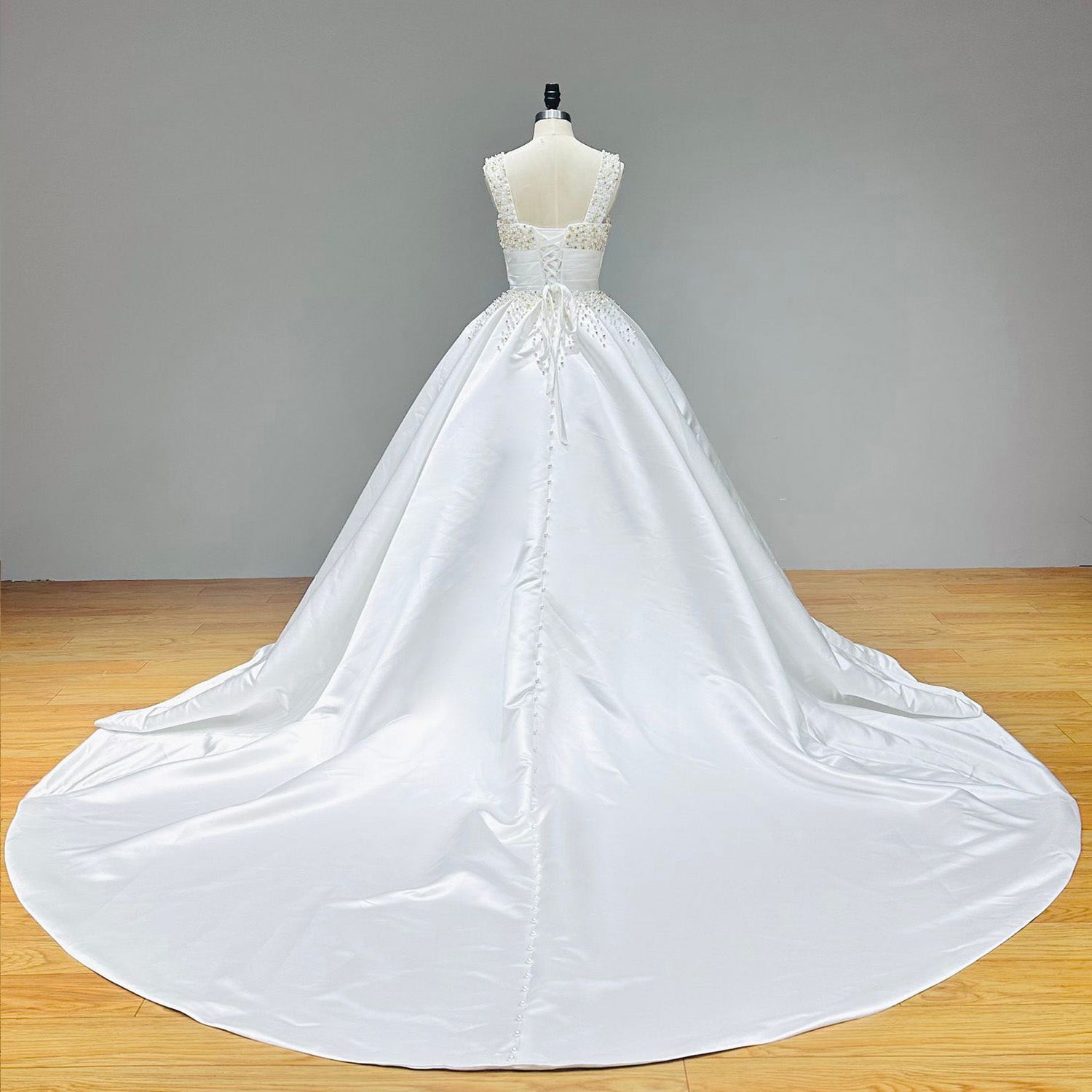 Close-up detail of a white bridal bodice highlighting alternating gold beads, silver crystals, and white pearls over a pleated satin wrap midriff closure on a mannequin.