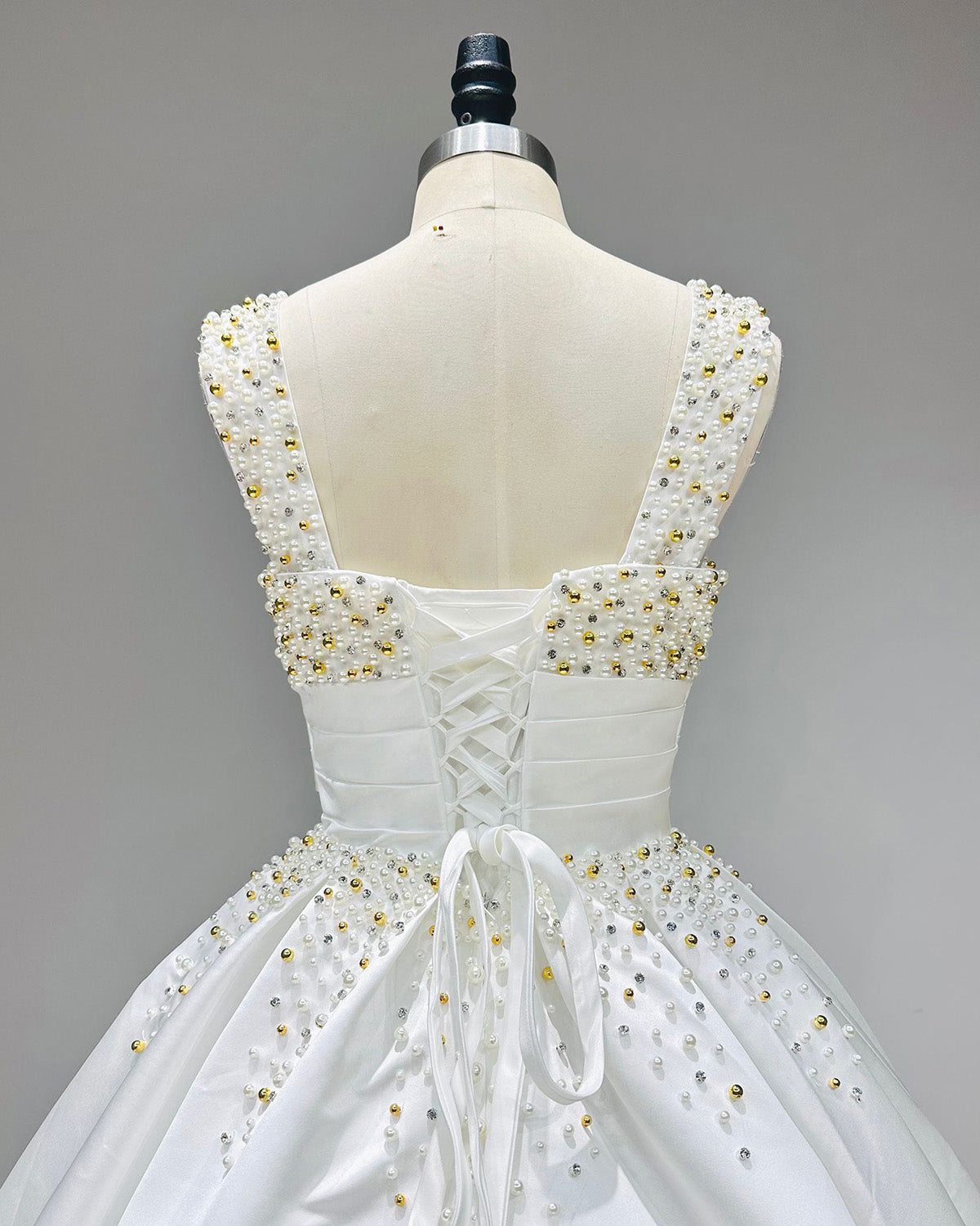 Detailed upper back view of a classic satin wedding gown on a mannequin, highlighting an adjustable satin ribbon lace-up corset closure framed by dense pearl beadwork.