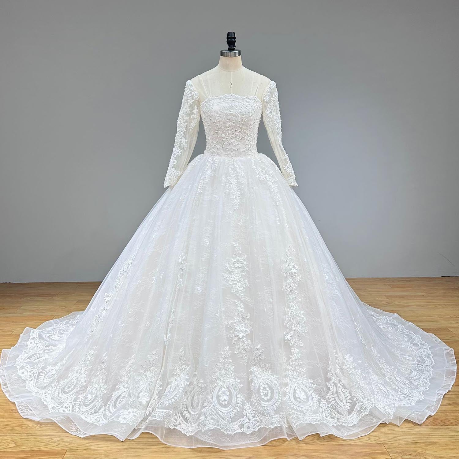 Full-length front view of a majestic white bridal ball gown on a dress form, highlighting the dense baroque lace motifs cascading down the voluminous tulle skirt.