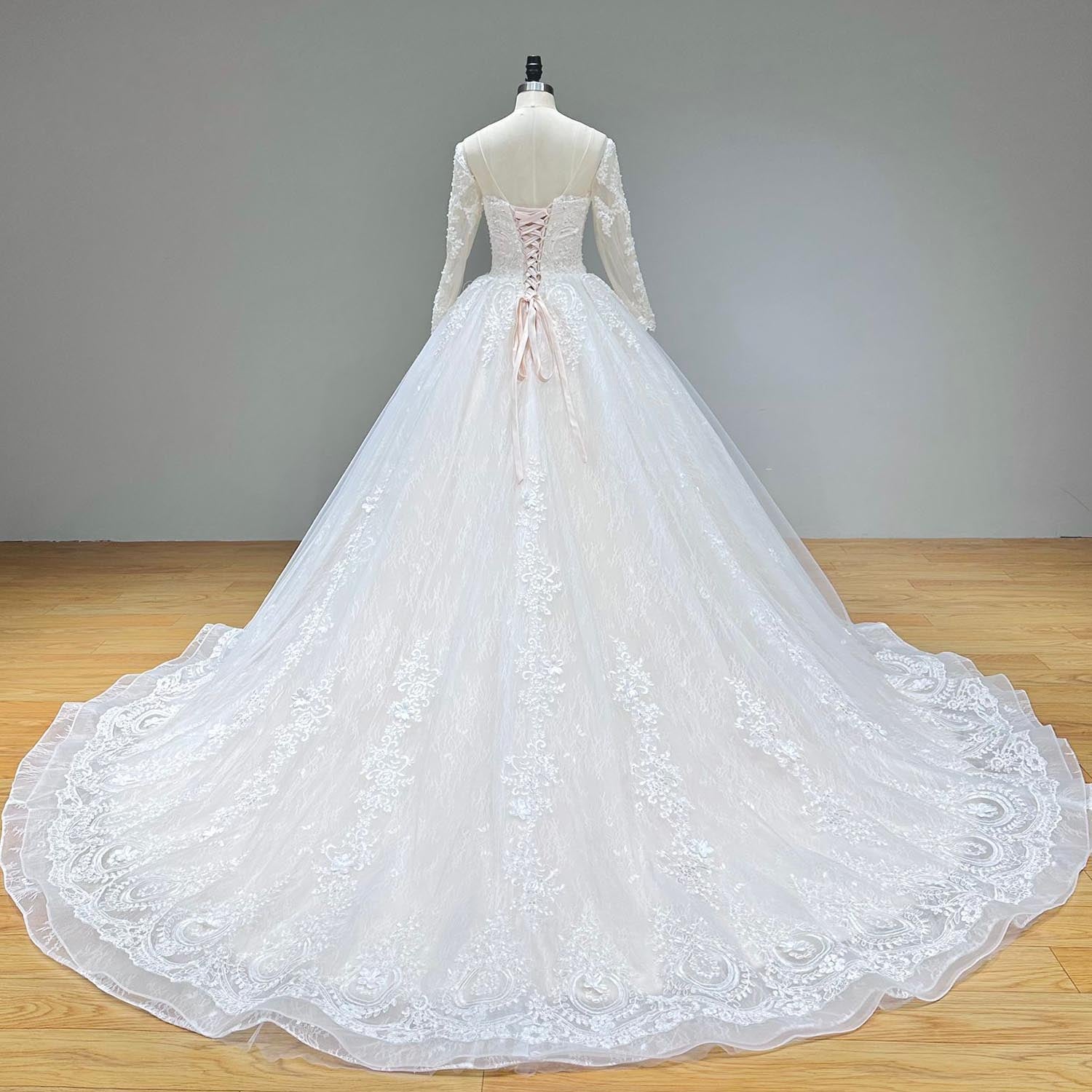 Studio back view of a modest long-sleeve wedding dress on a mannequin, showcasing a low dip back fitted with a soft pink satin lace-up corset closure and an extended train.