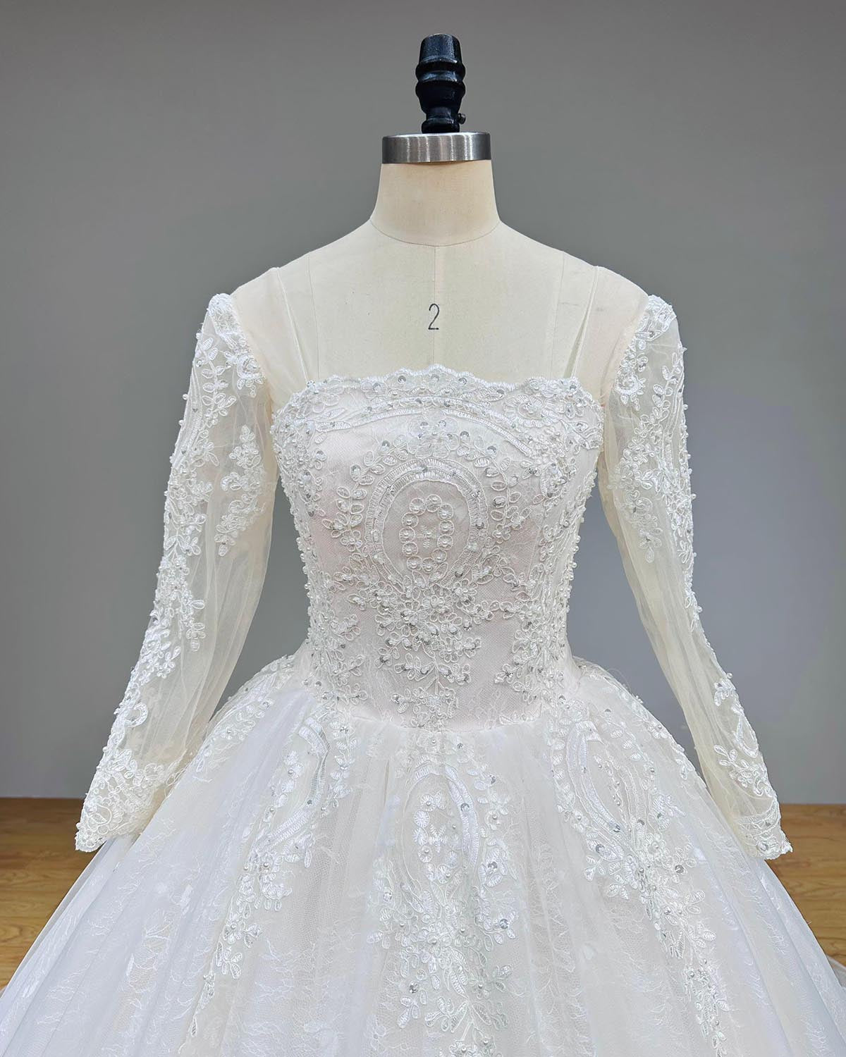 Macro close-up of a structured square-neck bridal bodice intricately detailed with symmetrical vintage beadwork, silver sequins, and sheer mesh long sleeves on a mannequin.