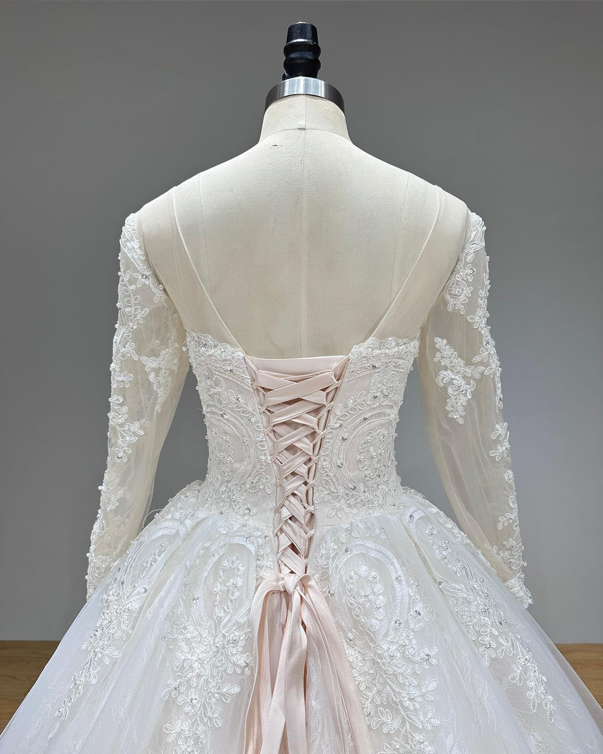 Detailed back perspective of a couture bridal gown bodice showcasing the adjustable ribbon corset ties over a sheer illusion panel framed by elegant lace embroidery.