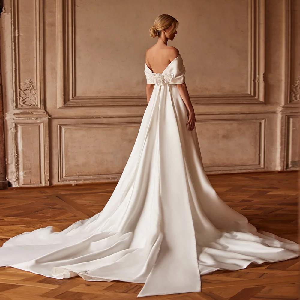 Full rear profile of a classic satin A-line bridal gown emphasizing the low back with hand-made floral details and a long pooling statement train.