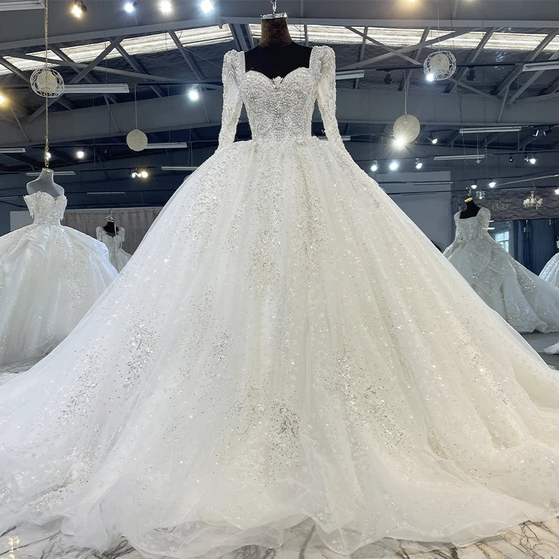 Model showcasing a romantic square neck bridal gown featuring intricate silver crystal embellishments and a voluminous layered organza skirt.