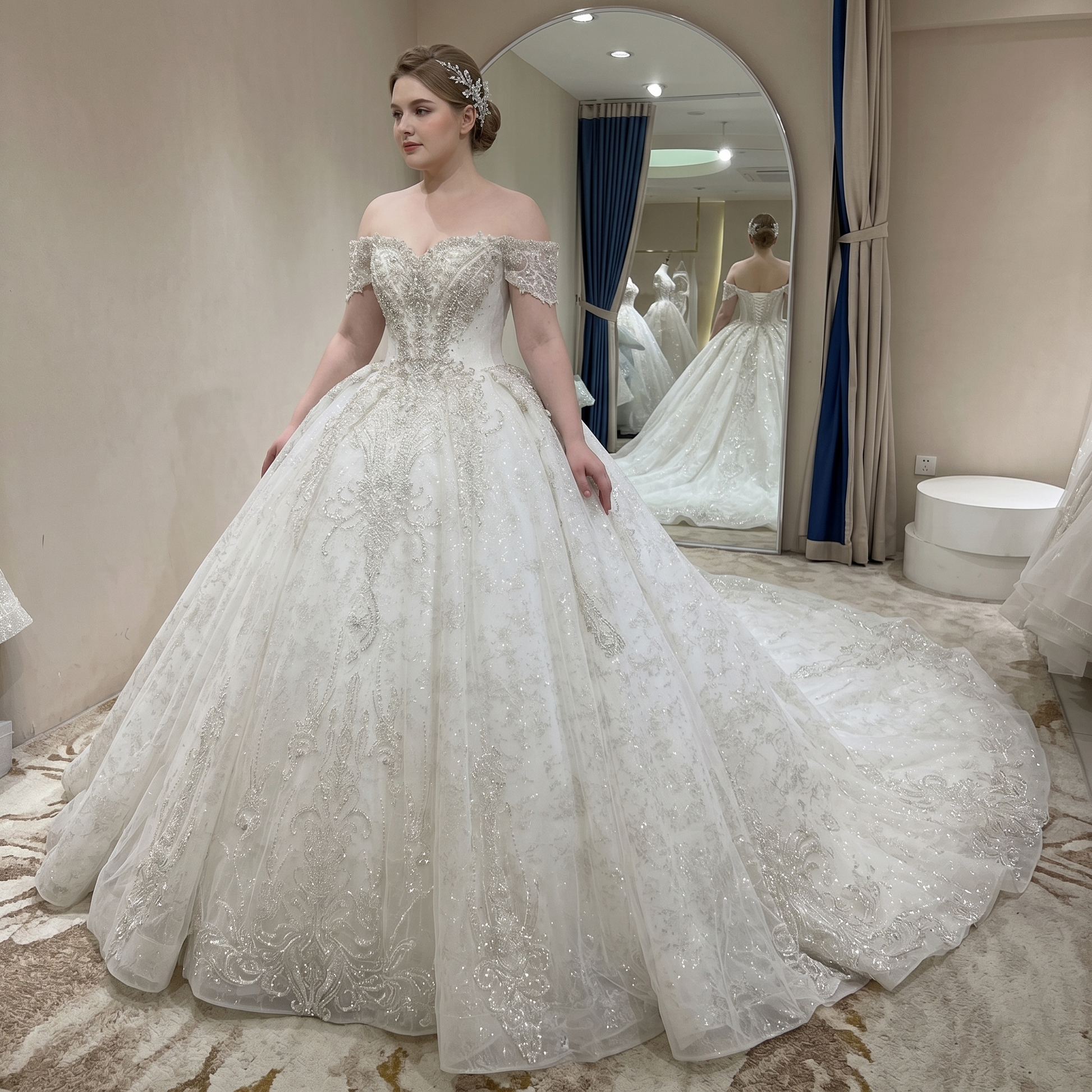 Rear view of an elegant bridal gown showcasing a long shimmering cathedral train and off-shoulder straps on a bride in a luxury showroom.