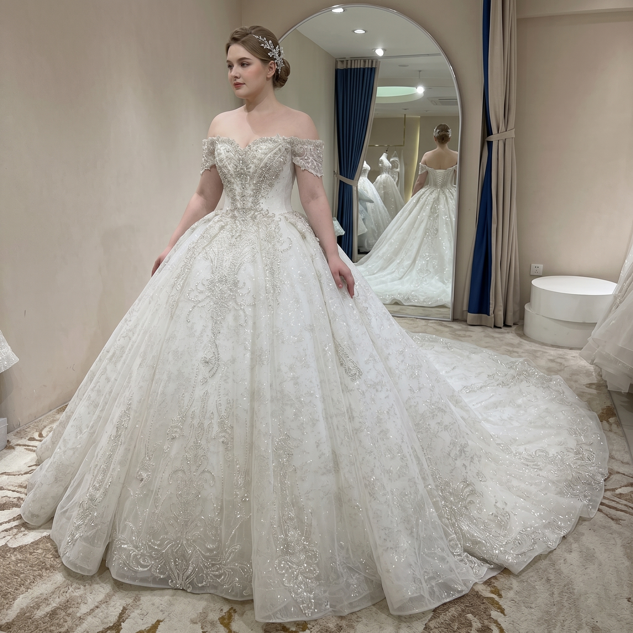 Rear view of an elegant bridal gown showcasing a long shimmering cathedral train and off-shoulder straps on a bride in a luxury showroom.