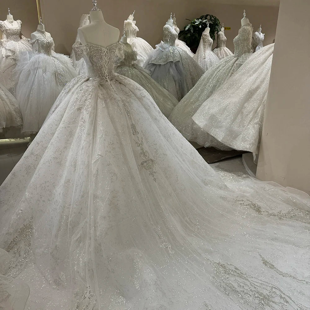 Side profile of a sleeveless ball gown wedding dress highlighting the massive scale of the long elegant train and reflective sparkling fabric.