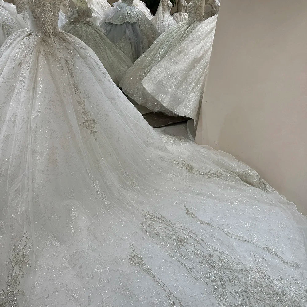 Shimmering white off-shoulder sleeveless ball gown wedding dress with a majestic princess silhouette and a grand long elegant train spread across a studio floor.