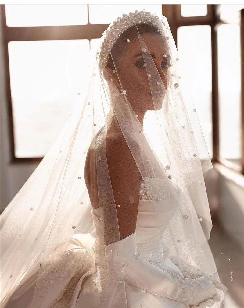 A bride wearing an elegant pearl-embellished veil and off-shoulder princess bridal gown with matching gloves.