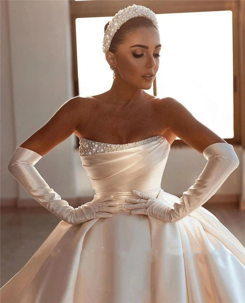 A portrait of a bride in an off-shoulder, pearl-detailed princess wedding gown with elegant satin opera gloves.