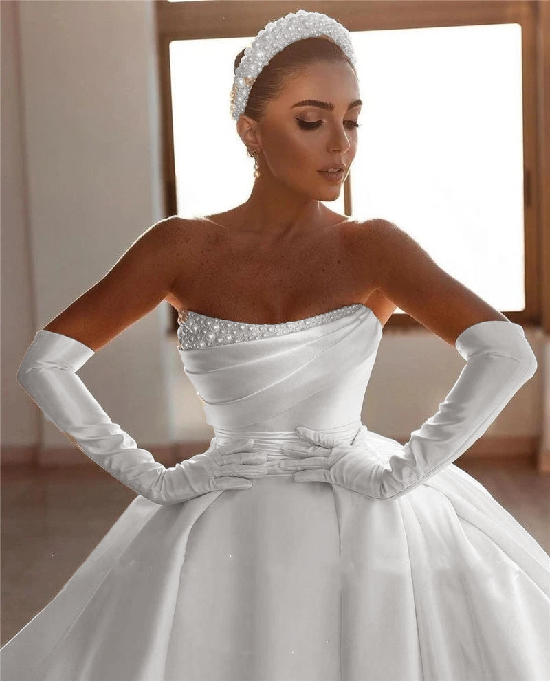 A close-up portrait of a bride wearing an off-shoulder princess bridal gown with intricate pearl accents on the bodice and matching opera gloves.
