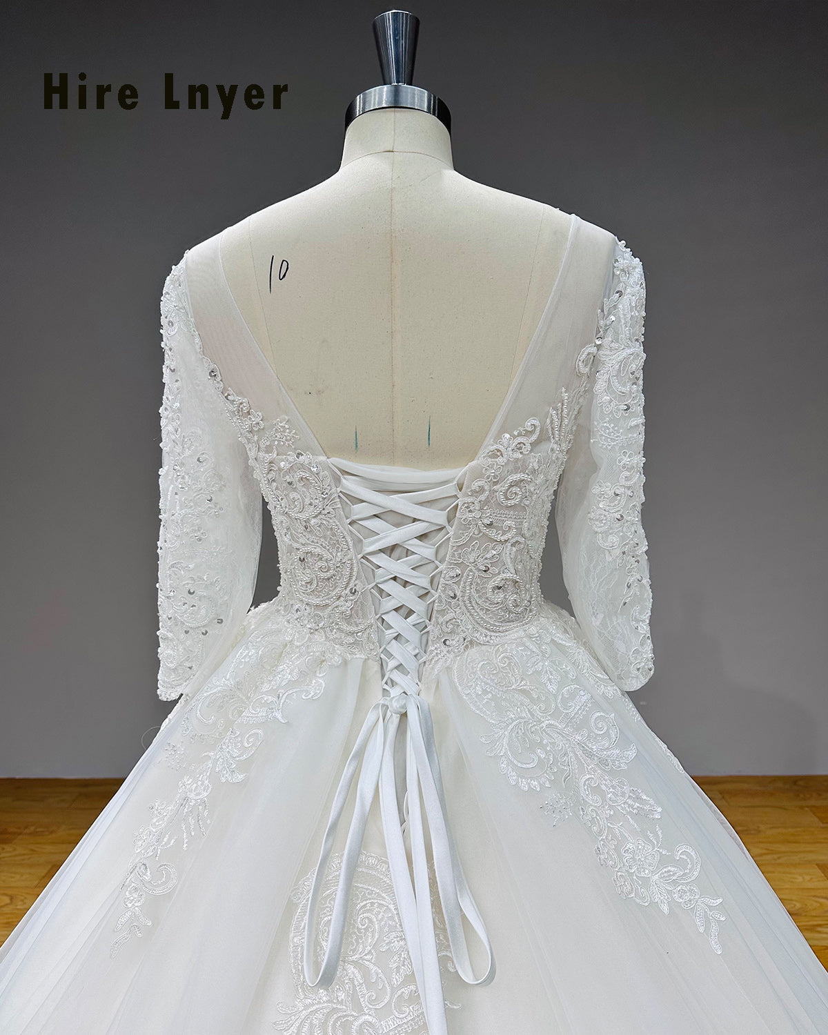Detailed rear view of a bridal gown on a dress form showcasing a traditional white lace-up corset closure and heavily beaded mesh sleeves.
