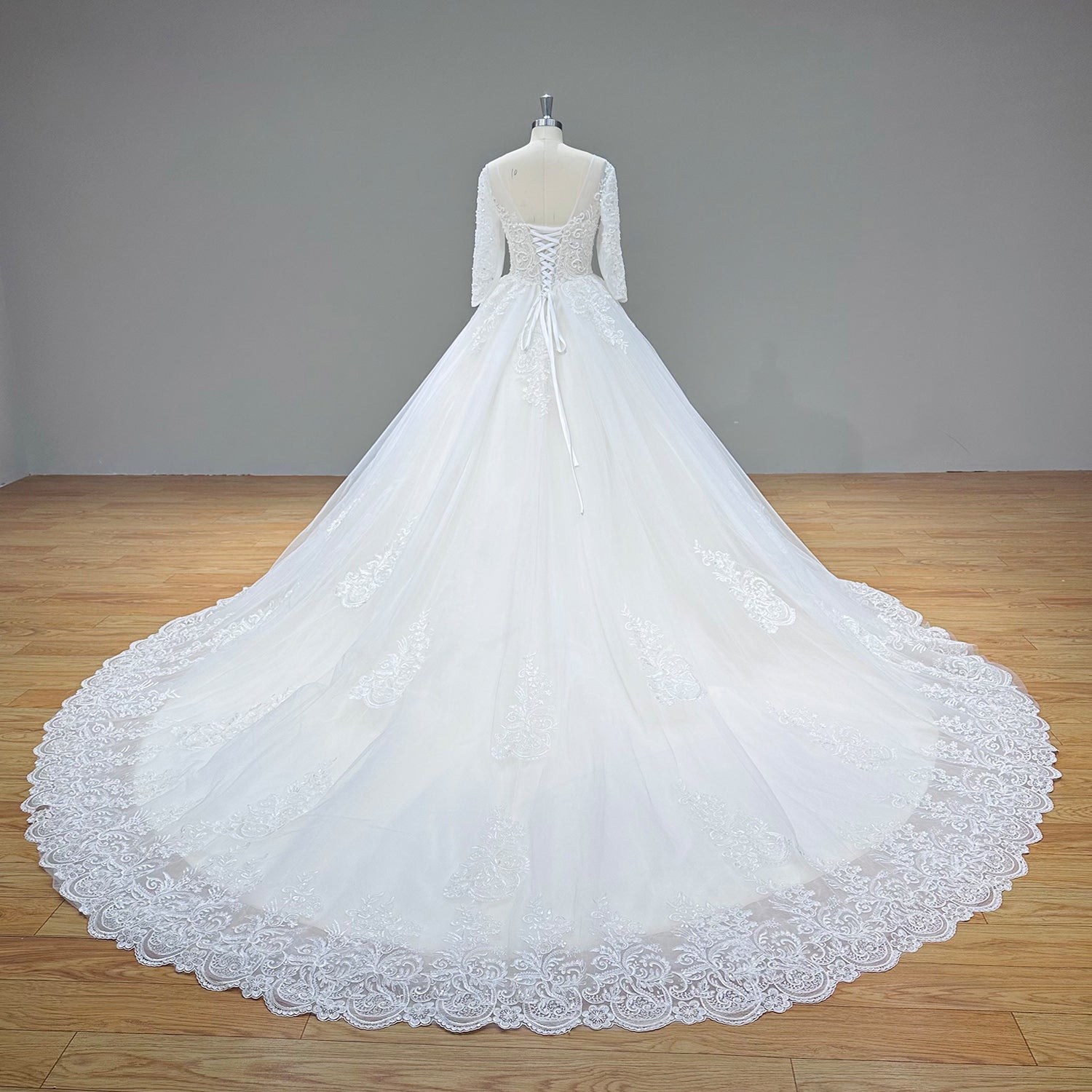 Full-length back view of an ivory half-sleeve ball gown wedding dress on a mannequin, showcasing the adjustable lace-up corset closure and an expansive cathedral train with a scalloped lace border.