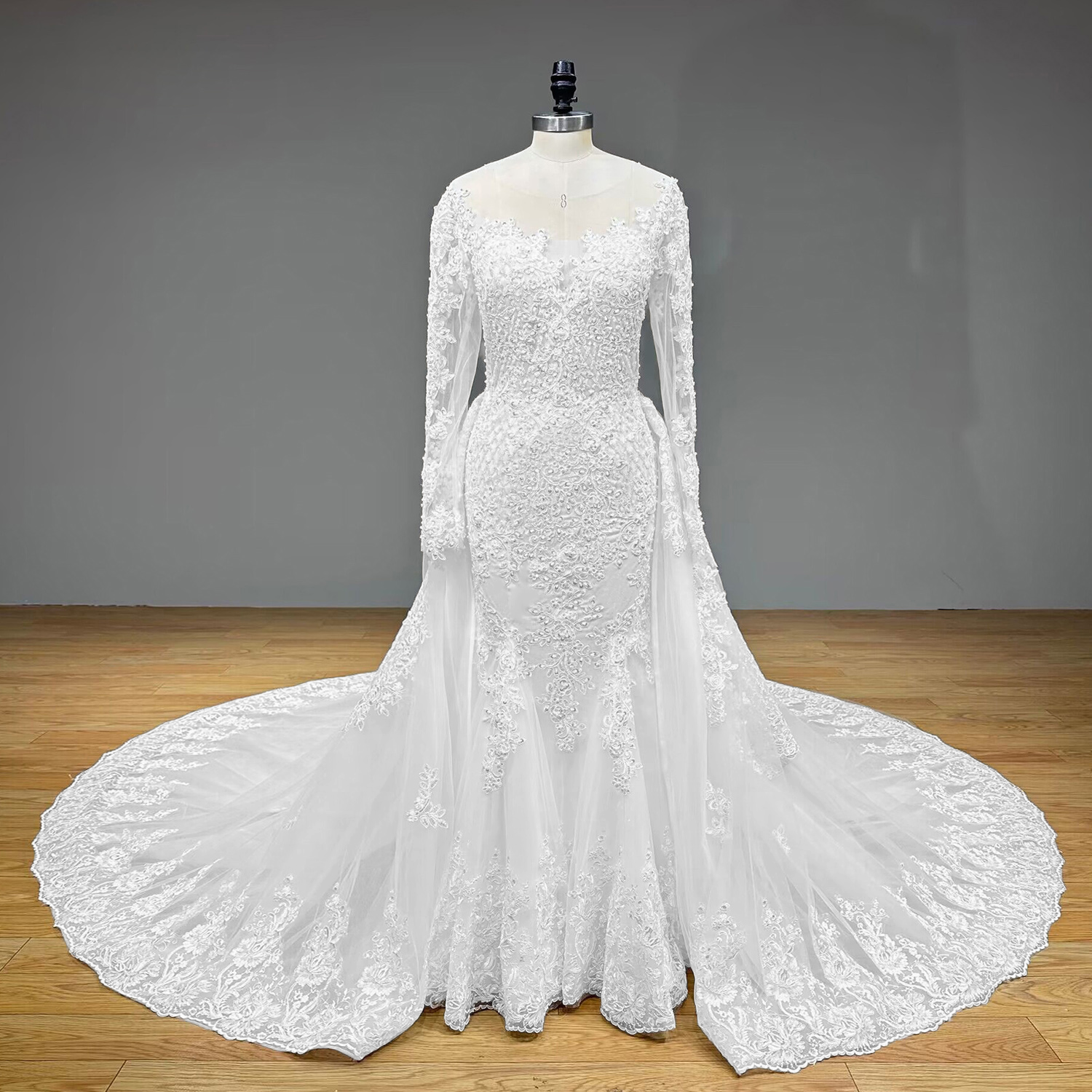Full-length front view of a luxury lace wedding dress on a mannequin, featuring a form-fitting silhouette with an illusion neckline, detailed embroidery, and a dramatic pooling tulle overskirt train.