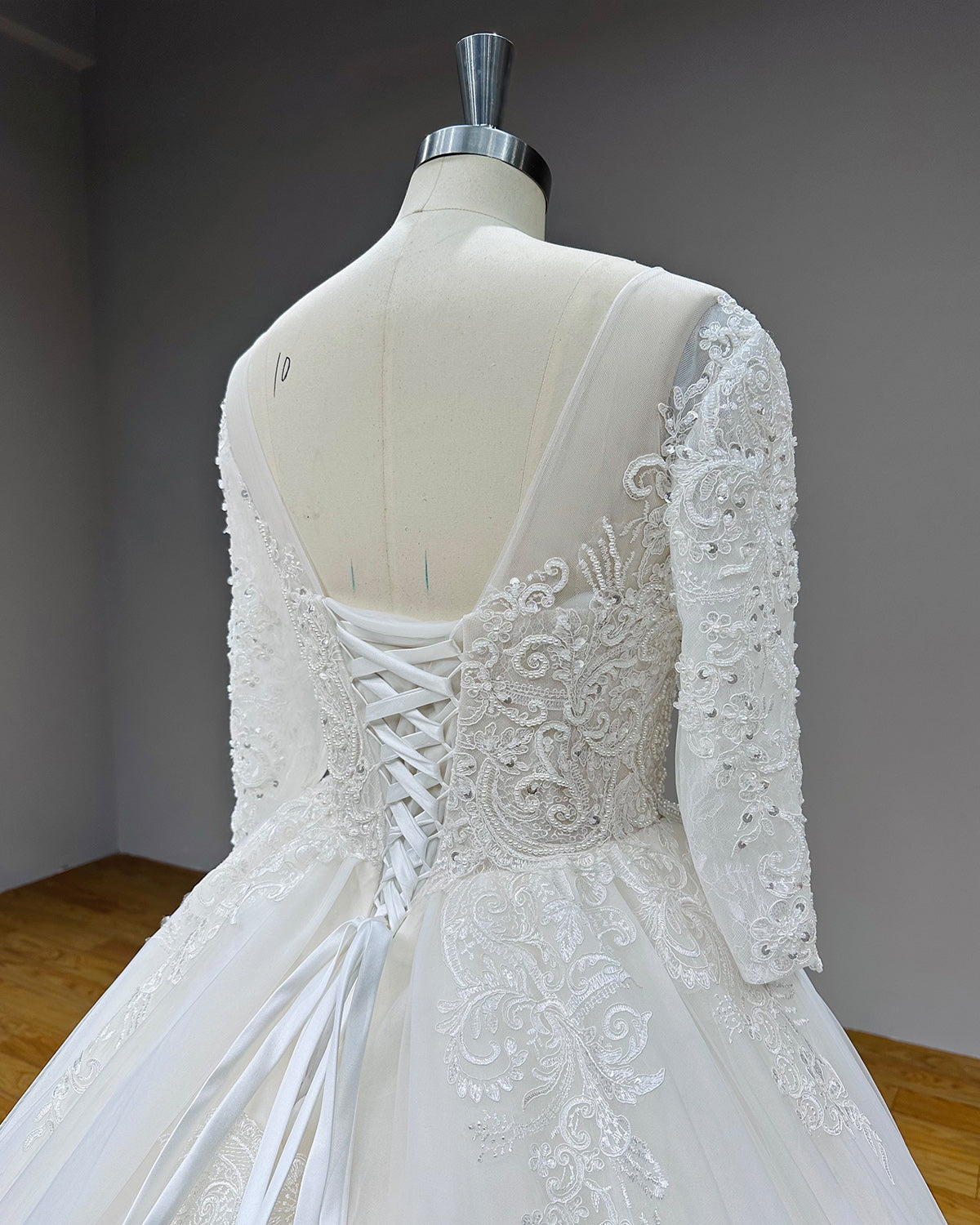 Close-up back view of a wedding dress bodice showing the adjustable satin ribbon lace-up corset back and sheer V-neck border embedded with pearls.