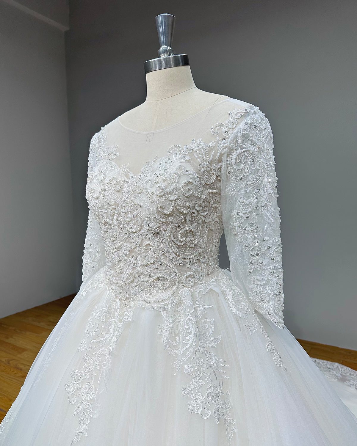 Close-up side profile view of a bridal bodice highlighting the intricate swirl embroidery, pearl appliques, and a sheer illusion neckline overlay.