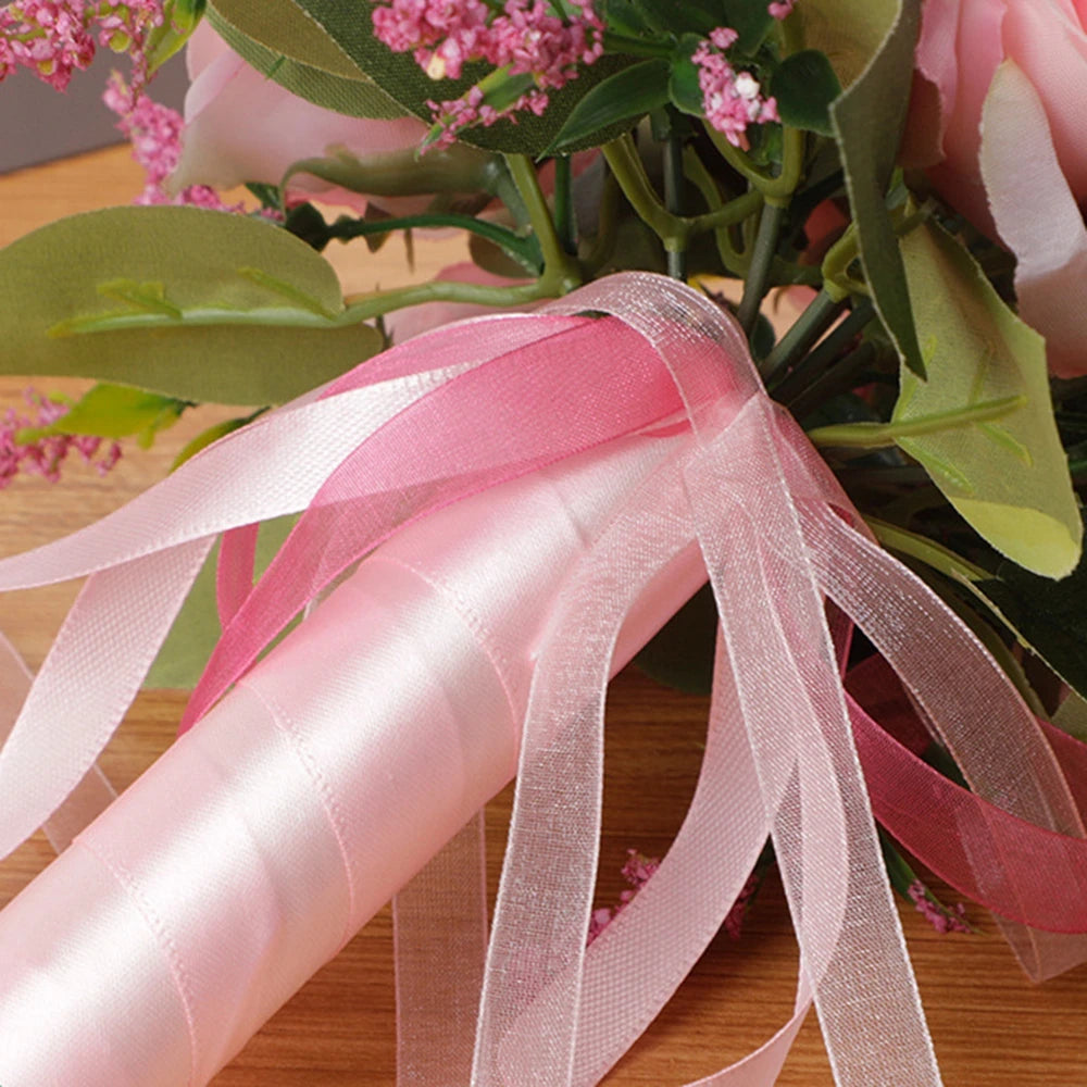 Detailed close-up macro view of a bridal bouquet handle wrapped tightly in pink satin ribbon with hanging sheer organza streamers.