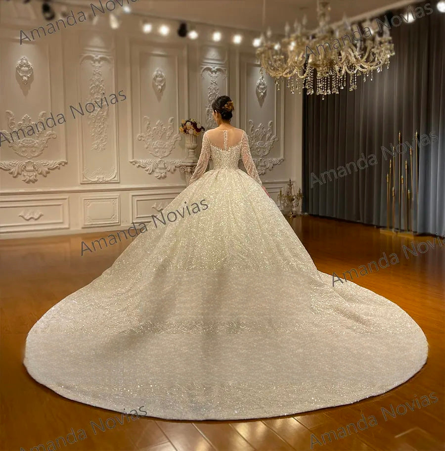 Back view of a sparkly long sleeve wedding dress showcasing a sheer illusion back with button details and an expansive circular cathedral train.