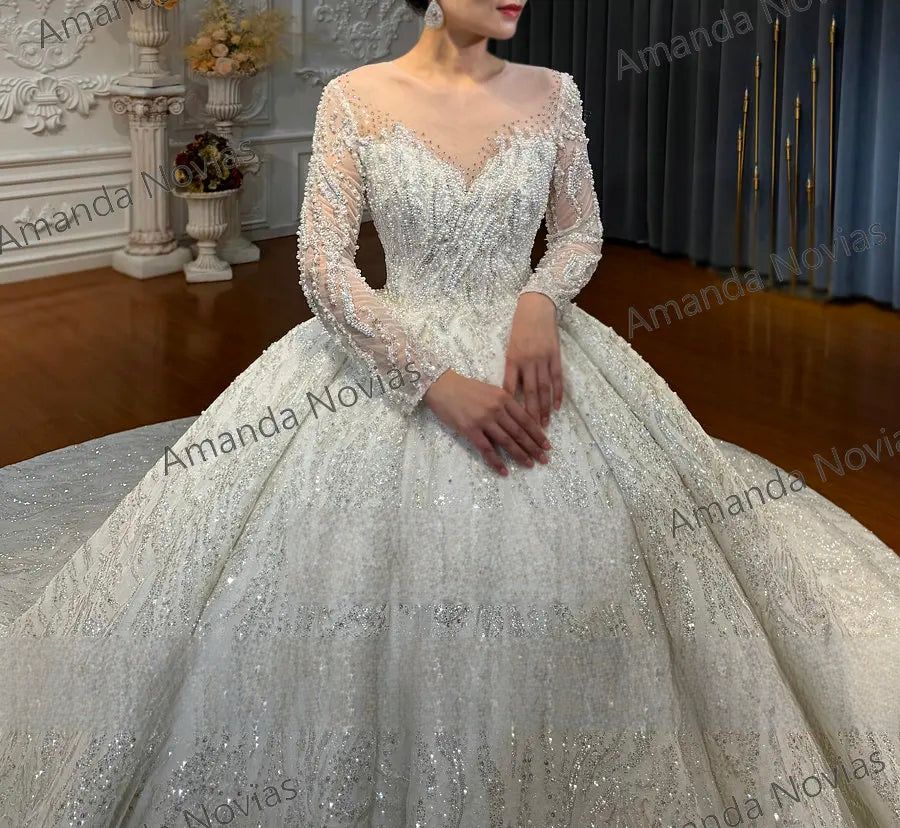 Close-up detail of a wedding dress bodice featuring intricate crystal beadwork, floral lace appliques, and a delicate sheer V-neckline with long sleeves.
