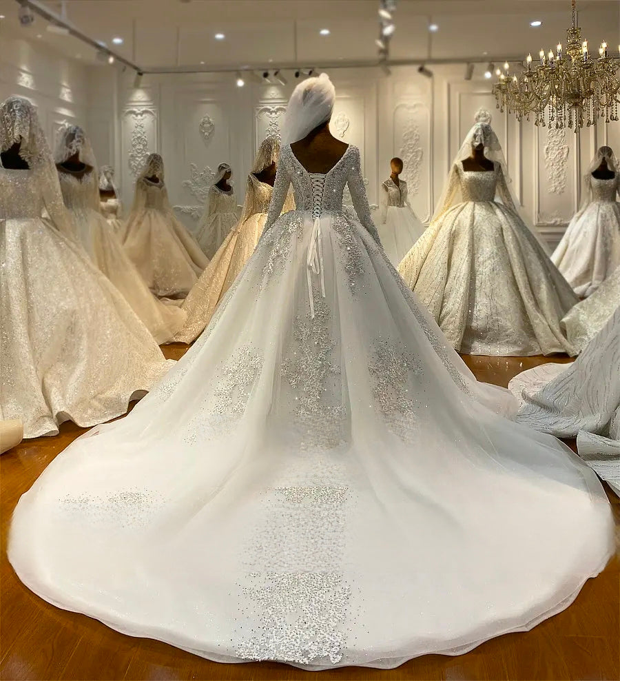Full rear view of a luxury bridal ball gown showcasing a majestic cathedral-length train adorned with heavy pearl beading and intricate lace appliques on a sparkling off-white fabric.