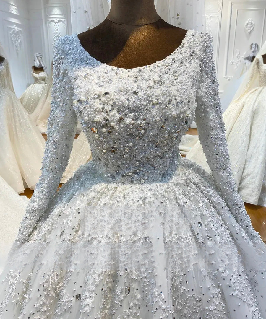 Macro close-up of the front bodice on a heavy beaded pearl wedding dress, showcasing the intricate craftsmanship of hand-sewn pearls, sparkly crystals, and 3D floral lace appliques.